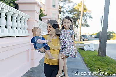 Beautiful mother carrying her happy young daughters in peaceful neighborhood Stock Photo