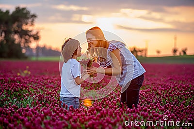 Beautiful mother and son in crimson clover field, mom getting bouquet of wild flowers gathered from her child for Mothers day Stock Photo