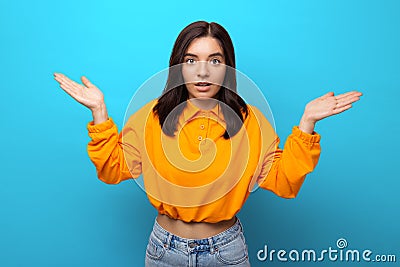 Beautiful multiethnicity woman in orange trendy shirt surprised expression against blue background Stock Photo