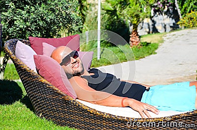 Beautiful Muscular tanned smiling man with sunglasses posing and relaxing in a tropical garden Stock Photo