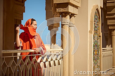 Beautiful Muslim woman standing between marble columns, looking into the distance, while wind blowing shawl on her head Stock Photo