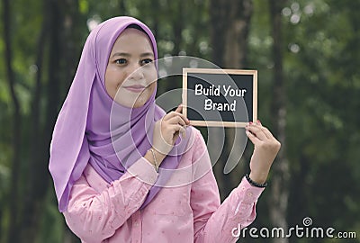 Beautiful muslimah stand and holding chalkboard with word BUILD YOUR BRAND. Stock Photo