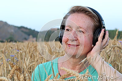 Beautiful Natural Mature Woman with Headphones Outdoors. Enjoying Music with Copy Space Stock Photo