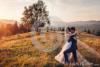 Beautiful newlyweds couple hugging in mountains at sunset. Bride and groom walking in summer Carpathians. Stock Photo