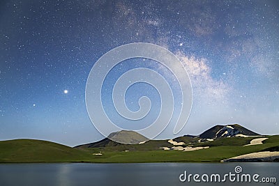 Beautiful night landscape. Alpine lake in the old volcanic mountains and beautiful bright milky way galaxy. Stock Photo