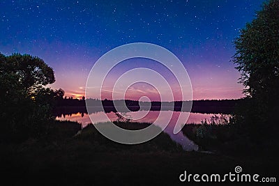 Beautiful night landscape on the forest lake with stars and reflected clouds in water in spring. Colorful sky. Nature background Stock Photo