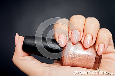 Beautiful Nude manicure with gold decor. Womens hand holding a bottle of nail Polish Stock Photo
