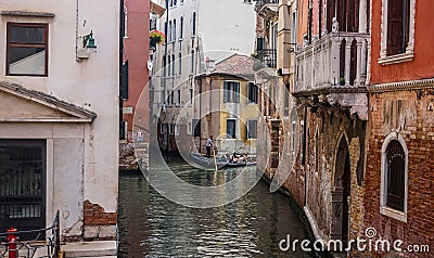 Beautiful old venetian street with old shabby colorful buildings and tourists in gondola. Editorial Stock Photo