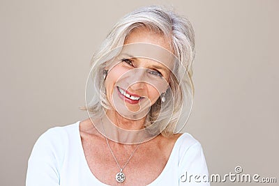 Beautiful older woman smiling and standing by wall Stock Photo