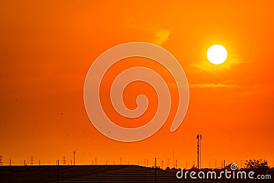 Beautiful orange sunset sky with roof of factory and birds flying near high voltage electric pylons. Evening sunset sky at Stock Photo