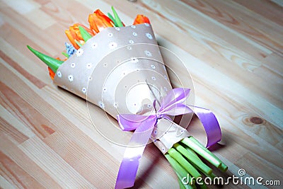 Beautiful orange tulips bouquet in wrapping paper with ribbon on wooden table Stock Photo