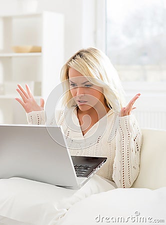 Beautiful outraged woman sitting on the sofa using a laptop Stock Photo