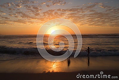 Beautiful and peacful sunset over ocean and beach with silhouette of 2 children playing Stock Photo