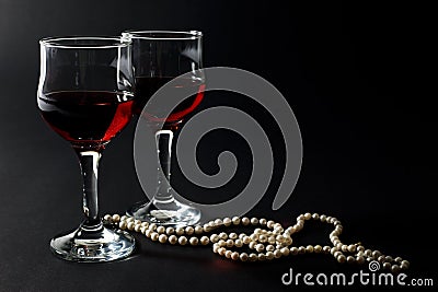 Beautiful Pearl Necklace and Two Glass Cups of Red Wine Isolated on Black Stock Photo