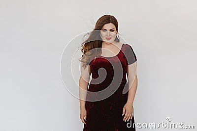 Beautiful plus size model girl in modish red velvet dress isolated at white background. Young fat woman with bright Stock Photo