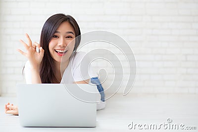 Beautiful portrait asian young woman working online laptop with excited lying on floor brick cement background, freelance girl Stock Photo