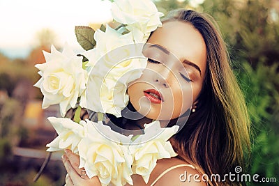 Beautiful portrait of a girl with white roses. Girl holds a bouquet of gorgeous roses near her face. Unification with nature, love Stock Photo