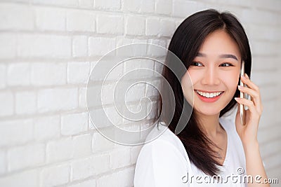 Beautiful of portrait young asian woman talk smart phone and smile standing on cement brick background Stock Photo