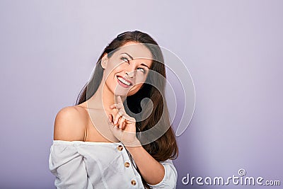 Beautiful positive young casual woman with hand under the face thinking and looking up in white shirt on purple background Stock Photo