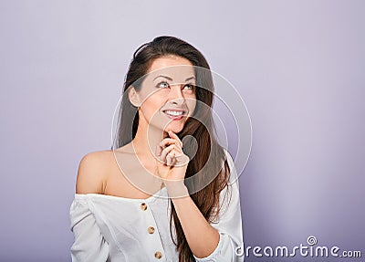 Beautiful positive young casual woman with hand under the face thinking and looking up in white shirt on purple background Stock Photo