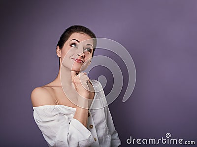 Beautiful positive young happy woman with hand under the face thinking and looking up in casual shirt on purple background Stock Photo