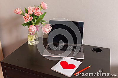 Beautiful postcard with a red heart, laptop and bouquet of pink tulips on the table. March 8, Valentine's day Stock Photo
