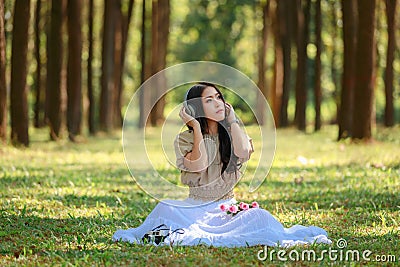 beautiful potrait asian woman siting and listening to headphone music in a pine forest and retro camera with rose flowers in frame Stock Photo