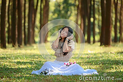 beautiful potrait asian woman siting and listening to headphone music in a pine forest and retro camera with rose flowers in frame Stock Photo