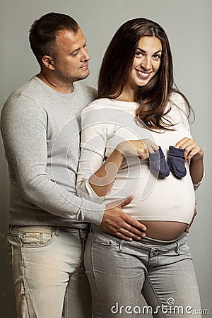 Beautiful pregnant couple hugging and smiling. Love and tenderness. The happiness of waiting. Gray background Stock Photo
