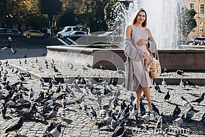 Beautiful pregnant mother stands near the pigeons in a sunny summer park. Walking on the street Stock Photo