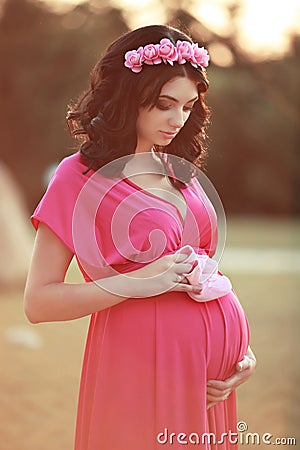 Beautiful pregnant woman holding baby's bootee over nature park Stock Photo