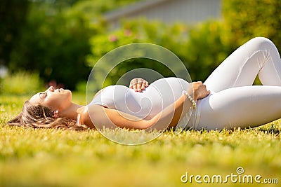 Beautiful pregnant woman in white clothes laying on grass Stock Photo