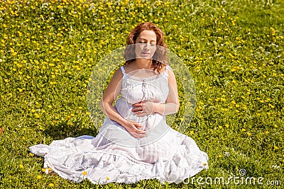 Beautiful pregnant woman in white dress relaxing in the green park in sunny day Stock Photo