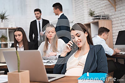 Beautiful pregnant woman speaks by phone in the office. Pregnancy at work. Stock Photo