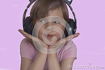 A beautiful preschool girl in wireless headphones smiles sweetly and listens to funny songs Stock Photo