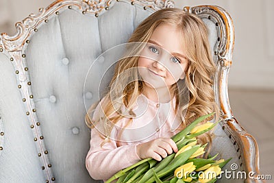 Beautiful pretty girl with yellow flowers tulips sitting in arm-chair, smiling. Indoor photo Stock Photo