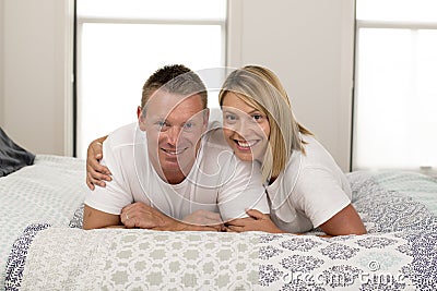 Beautiful and radiant couple smiling happy posing sweet lying on bed at home in successful husband wife relationship concept Stock Photo