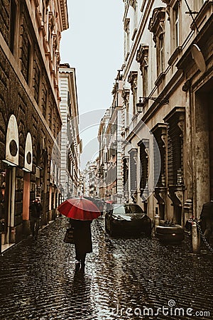 Beautiful rainy street of Rome with people under umbrella silhouettes for lifestyle design. Summer season. Dark and Editorial Stock Photo