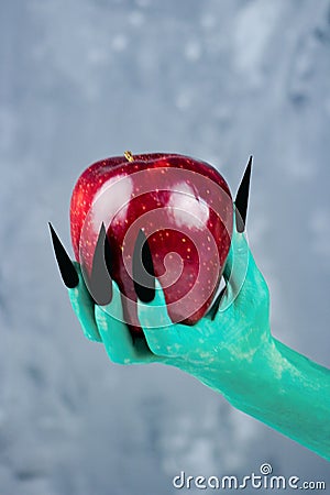 Beautiful red apple in green hands of old witch with black nails. Stock Photo