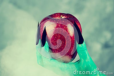 Beautiful red apple in green hands of old witch with black nails. Stock Photo