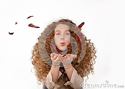 Beautiful redhaired curly long hair girl blowing feathers from hands. The concept of gentle care for skin, hair, softness and Stock Photo