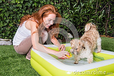 Beautiful red-haired woman plays with her dog by the pool Stock Photo