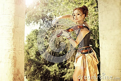 Beautiful redhair woman with body art on her face playing on violin outdoors. Stock Photo