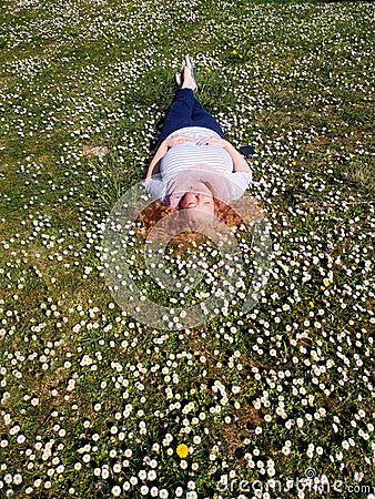 Beautiful redhead mature woman in her fifties lies contentedly in the grass and enjoys the sun in a field of daisies Stock Photo