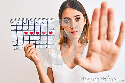 Beautiful redhead woman holding menstruation calendar over isolated background with open hand doing stop sign with serious and Stock Photo