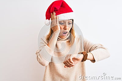 Beautiful redhead woman wearing christmas hat over isolated background Looking at the watch time worried, afraid of getting late Stock Photo