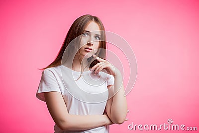 Beautiful redhead woman in white shirt looks up thoughtfully on pink background with copy space Stock Photo