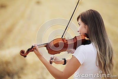 Beautiful romantic girl with loose hair playing the violin in the field Stock Photo