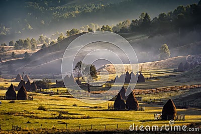 Beautiful rural mountain landscape in the morning light with fog, old houses and haystacks Stock Photo