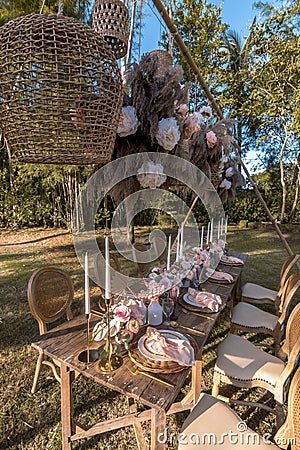 A beautiful rustic table setup at an outdoor garden wedding. White tall candles and pastel rose and tulip tabletop bouquet Stock Photo